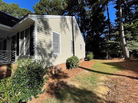 A house with a grey siding and a brown roof is surrounded by trees and bushes.