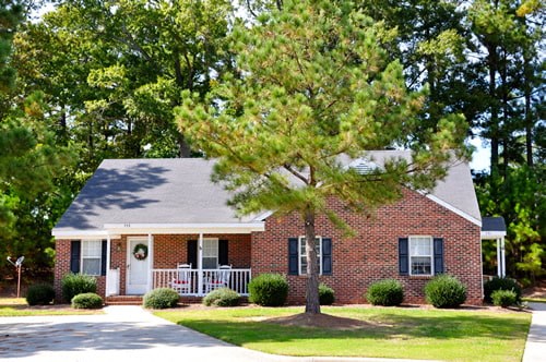 A small brick house with a white door and a tree in front.