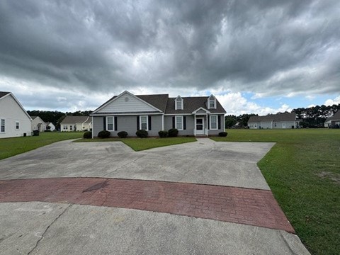 A house with a grey roof and white walls is surrounded by a driveway and a grassy area.