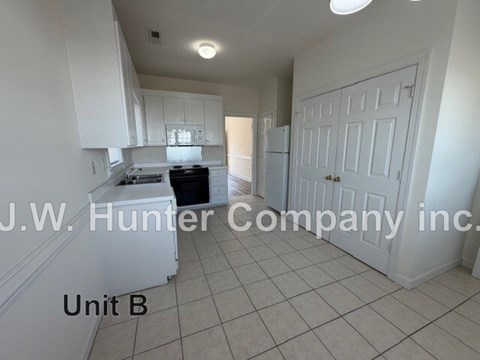 A kitchen with white cabinets and a white refrigerator in a white room.