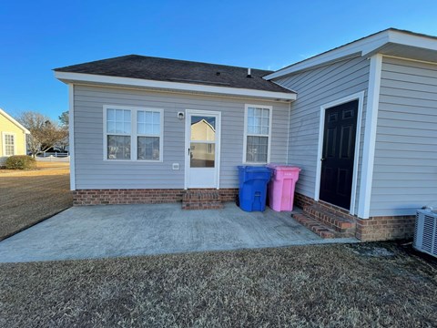 A house with a grey exterior has a blue and pink container outside.