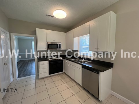 A kitchen with white cabinets and black countertops.