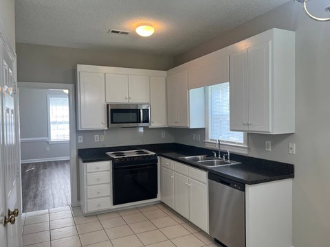 A kitchen with white cabinets and black countertops.