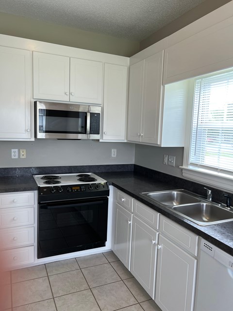 A kitchen with white cabinets and black countertops.