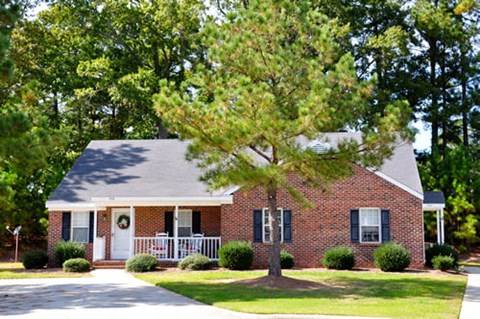A small brick house with a white door and a tree in front.