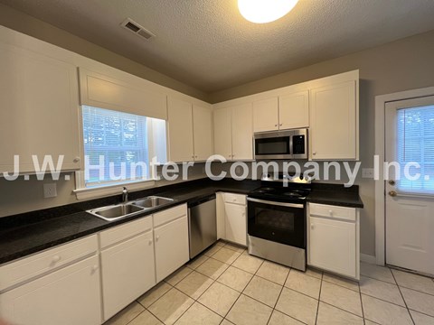 A kitchen with white cabinets and black countertops.