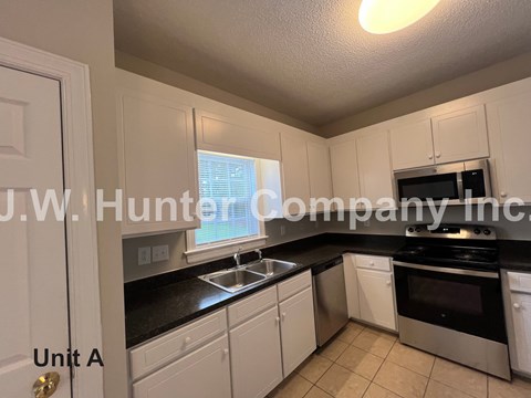 A kitchen with white cabinets and black countertops.