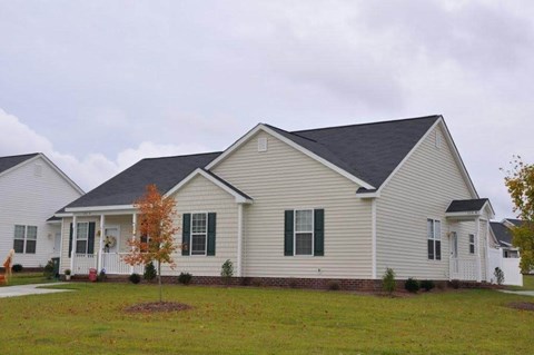 A house with a grey roof and white walls with a small tree in front.