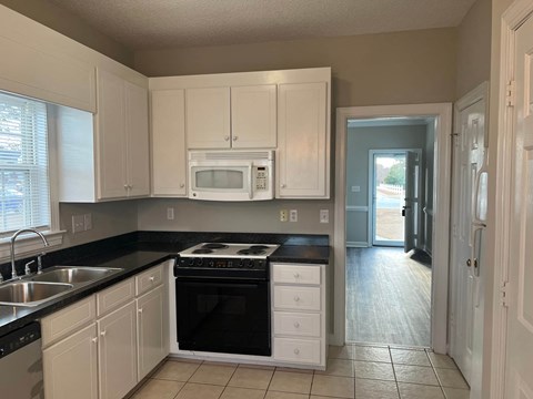 A kitchen with white cabinets and black countertops.