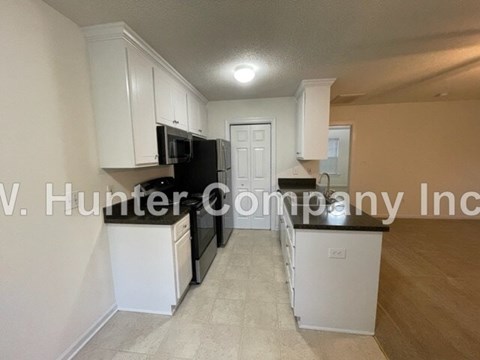 A kitchen with white cabinets and appliances, including a black refrigerator and microwave.