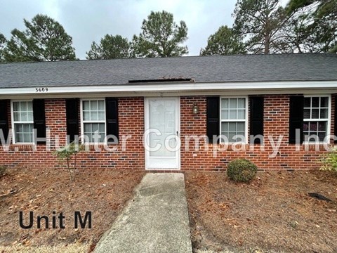 A brick house with a white door and windows with shutters.