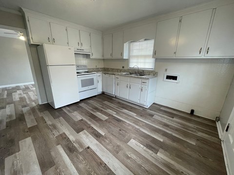 A kitchen with white cabinets and a wooden floor.