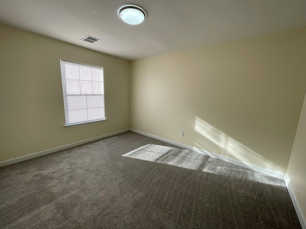A room with a carpeted floor, a window with blinds, and a ceiling light.