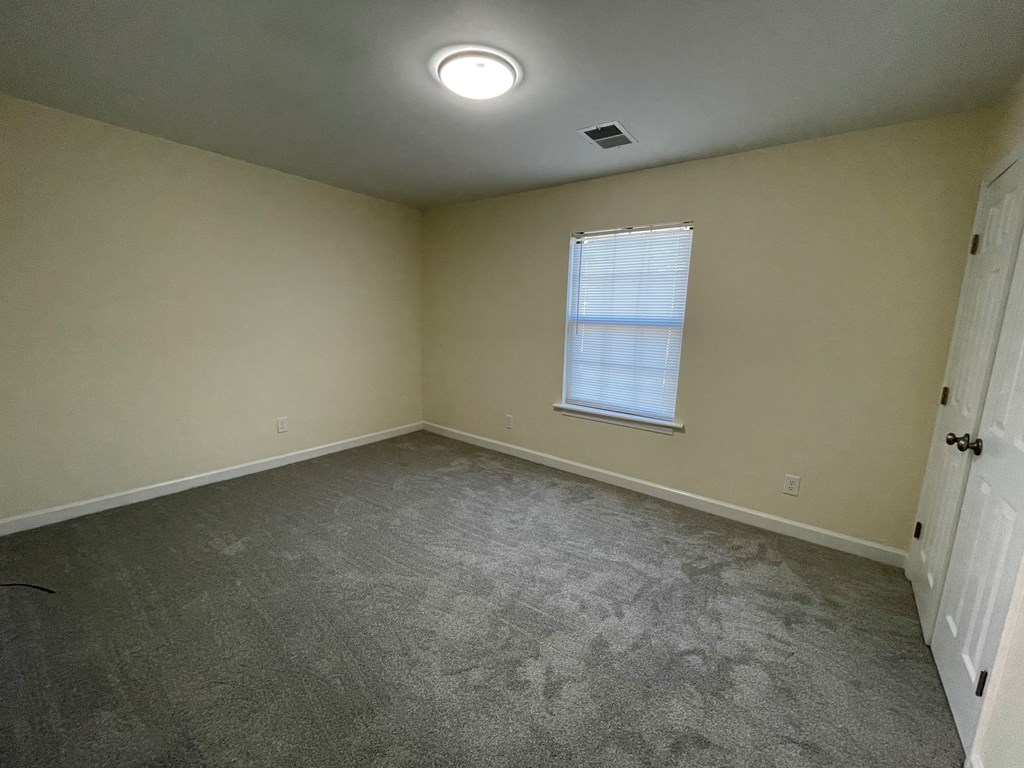 A room with a grey carpet and a window with blinds.