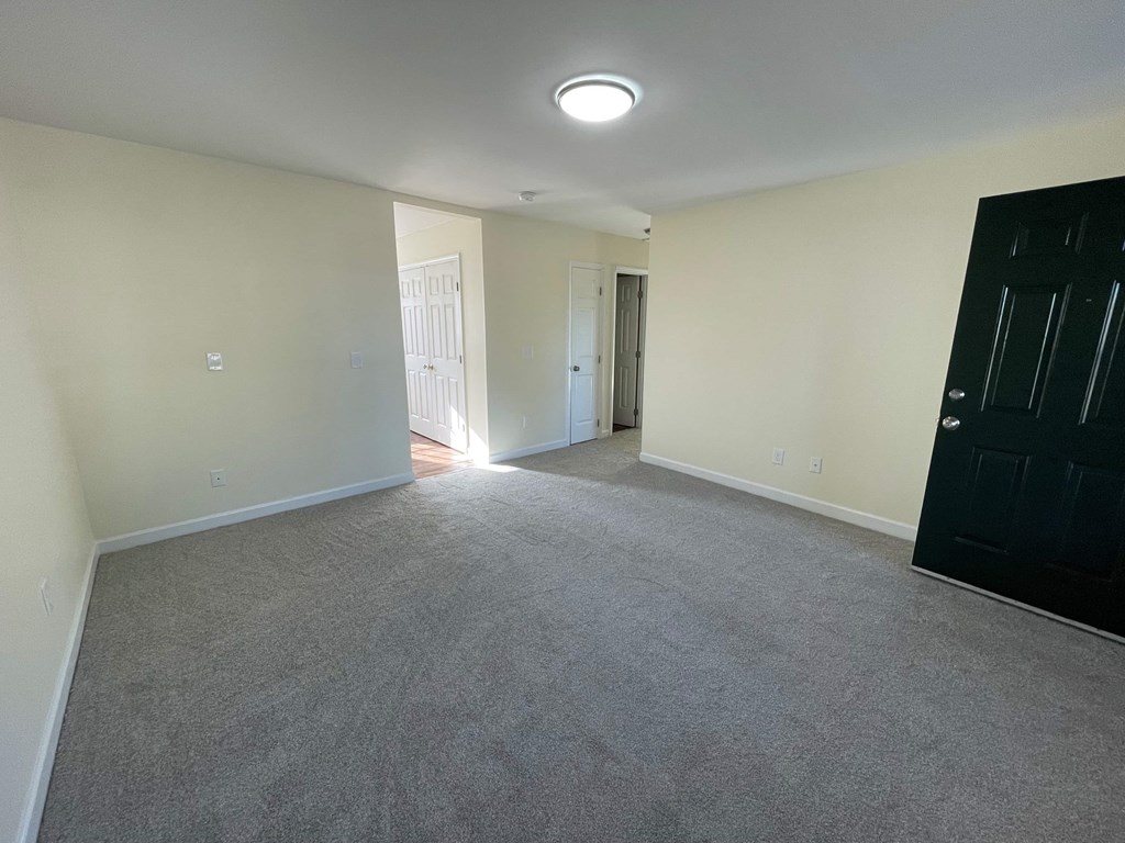 A room with a carpeted floor and a black door on the right side.
