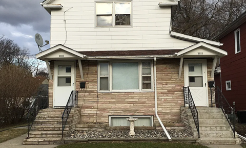 A two-story house with a white front and a brown brick wall.