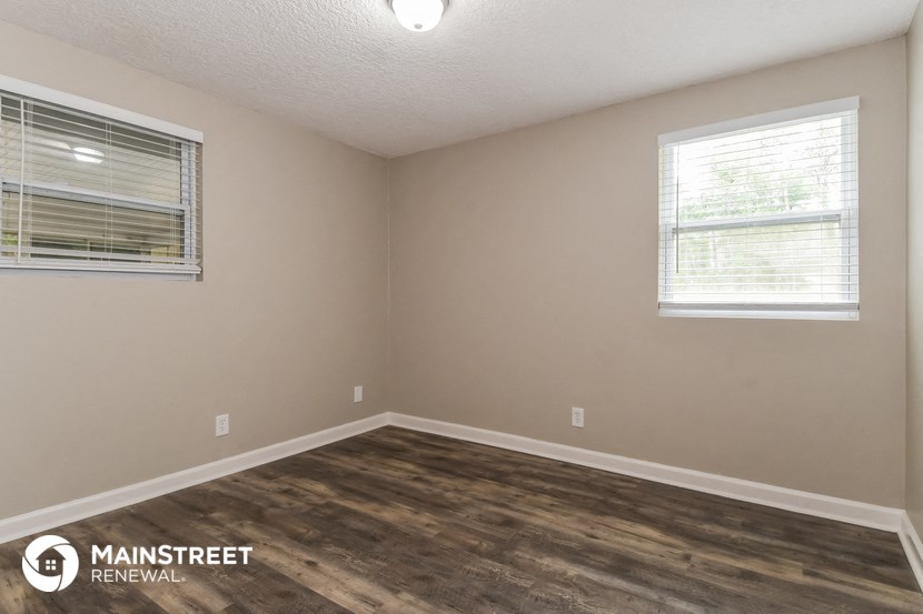 the interior of an empty room with wood flooring and two windows