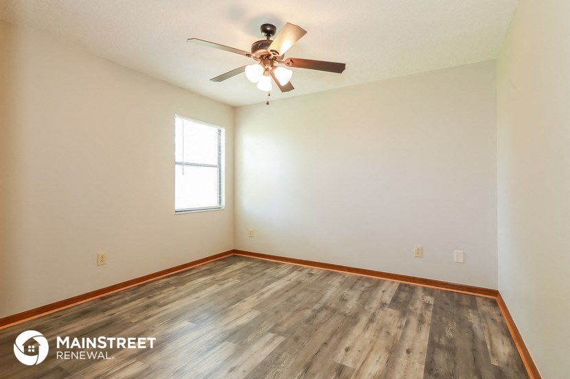 the spacious living room with wood flooring and a ceiling fan