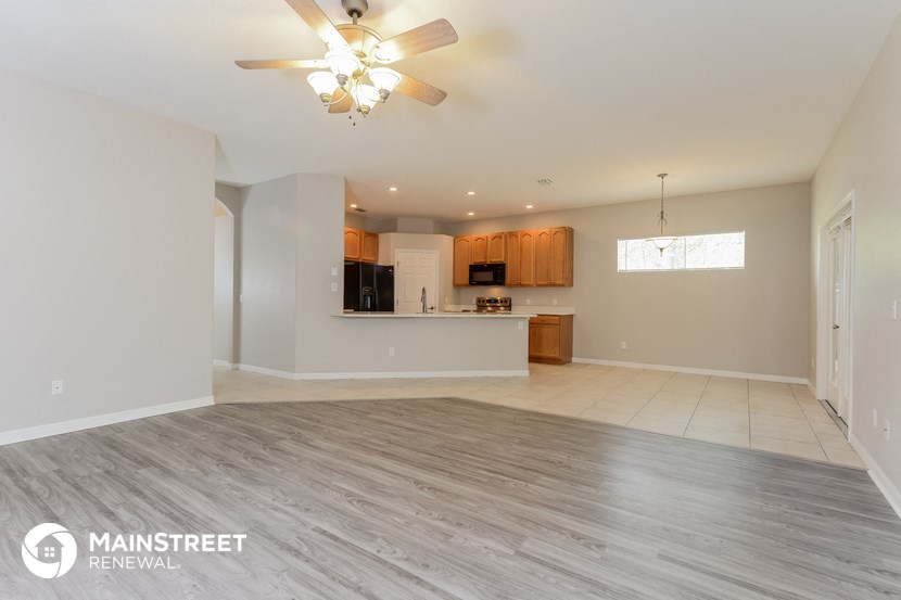 an empty living room with a ceiling fan and a kitchen