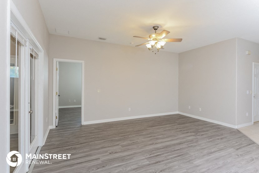 the living room of an apartment with wood flooring and a ceiling fan
