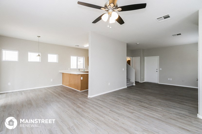 an empty living room with a ceiling fan and a kitchen