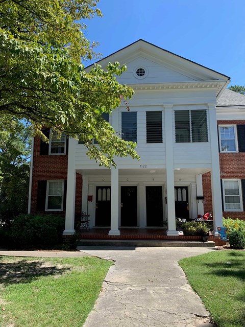 A white house with a porch and a tree in front.