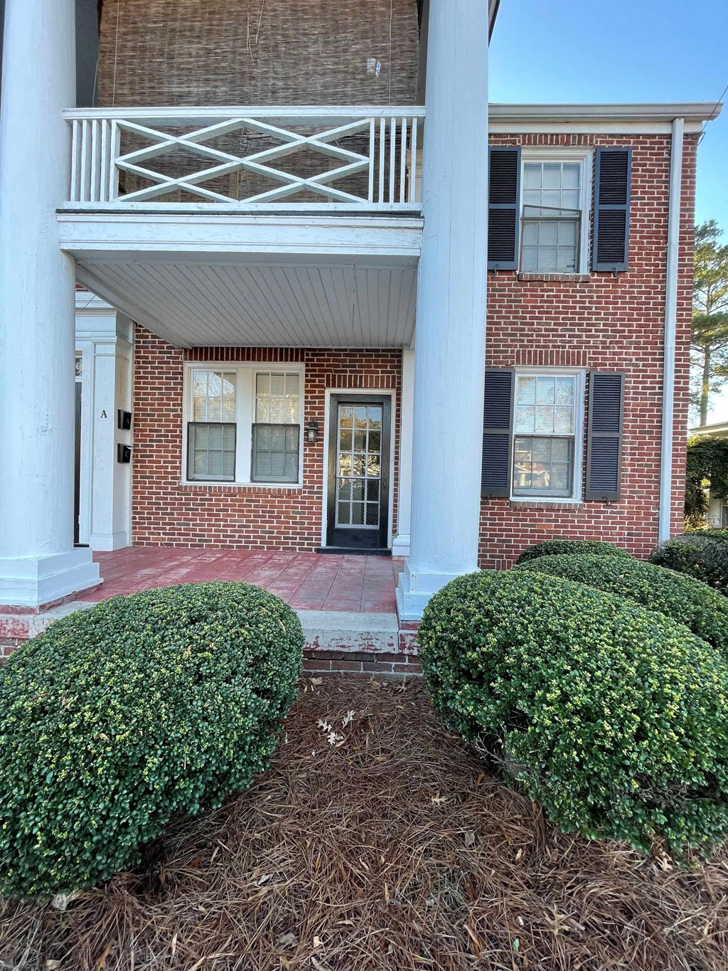A red brick house with a black door and a white porch.
