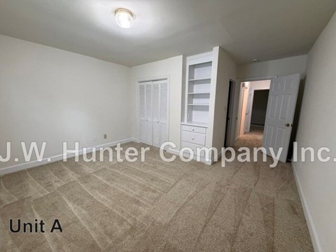 A room with carpeted floor and white walls, with a doorway leading to another room.