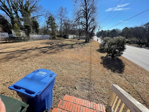 A blue recycling bin sits on a grassy area next to a brick wall.