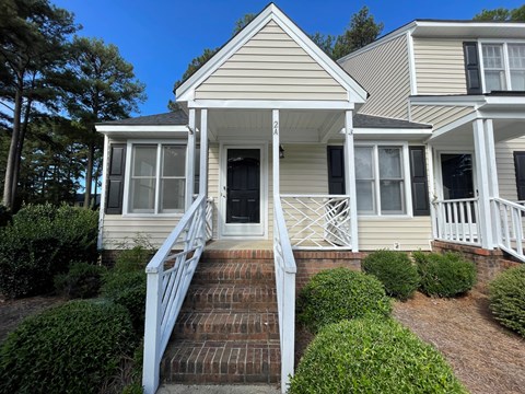 A house with a white porch and a brown staircase leading to the front door.