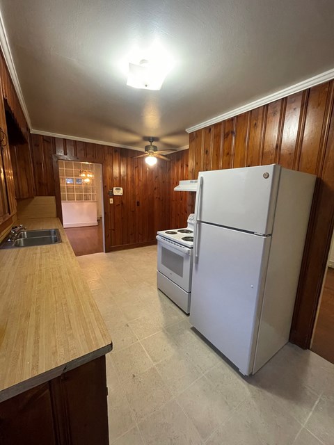 A white refrigerator is in a kitchen with wooden walls.