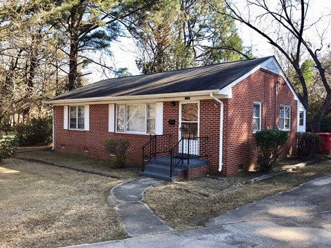 a small brick house with a front porch and a black staircase