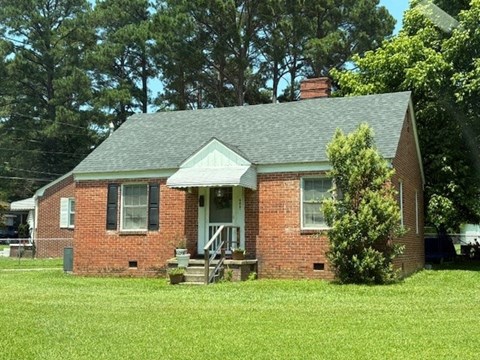 A small red brick house with a green roof and a white door.