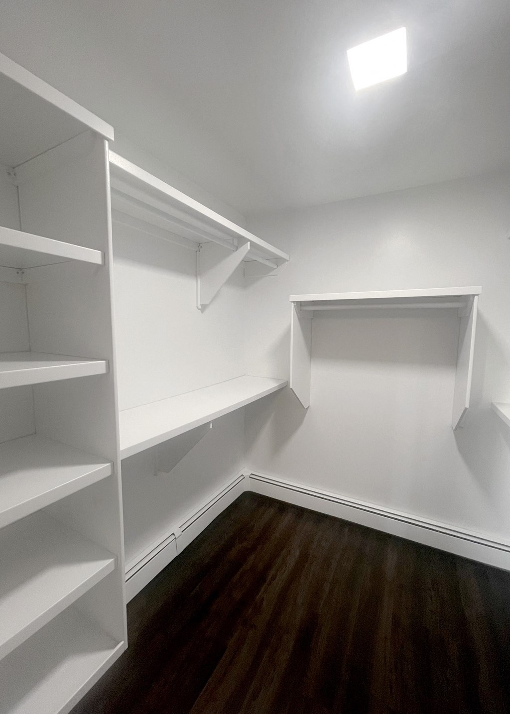 a walk in closet with white shelves and a wood floor
