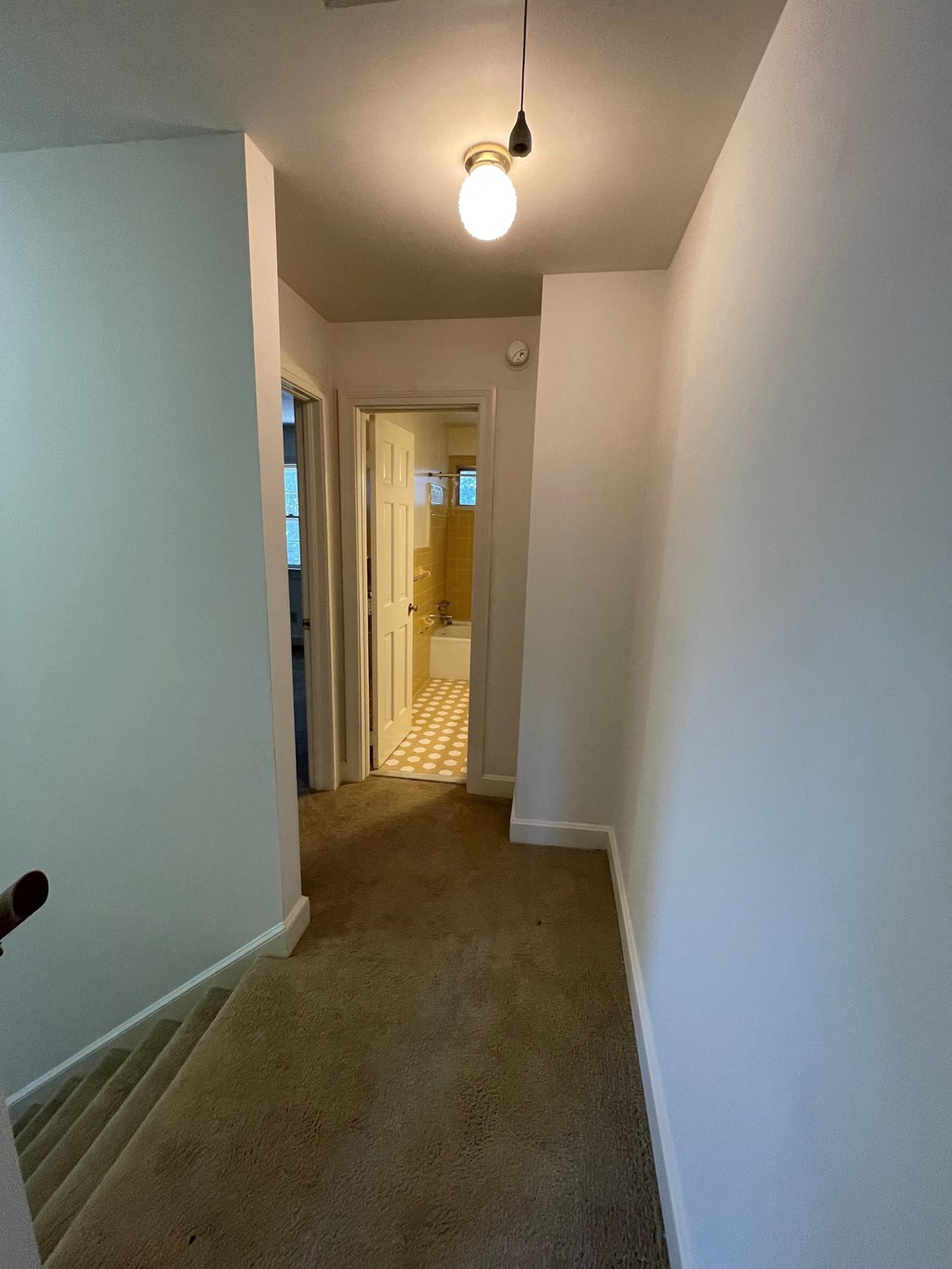 a hallway with a carpeted floor and a door to a bedroom and a bathroom
