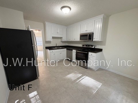 A kitchen with white cabinets and a black fridge is shown.