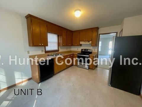 A kitchen with wooden cabinets and a black refrigerator is shown.