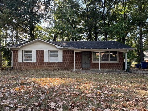 A small house with a brown roof and white trim is surrounded by fallen leaves.