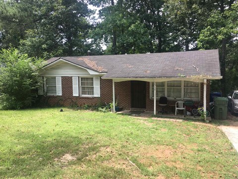a small brick house with a covered porch and a yard