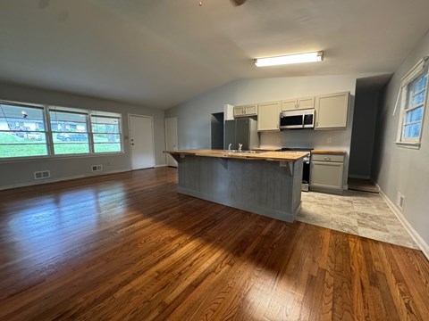 A large empty room with wooden floors and a kitchen area in the background.