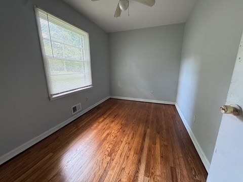 A room with wooden flooring and a window with blinds.