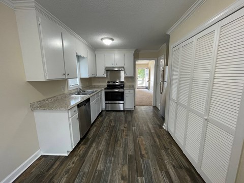 A kitchen with white cabinets and a wooden floor.