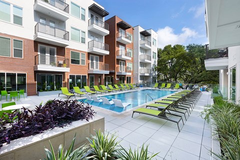 a swimming pool with green lounge chairs in front of an apartment building
