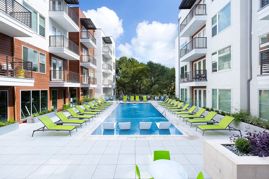 a swimming pool in the middle of apartments with green lounge chairs