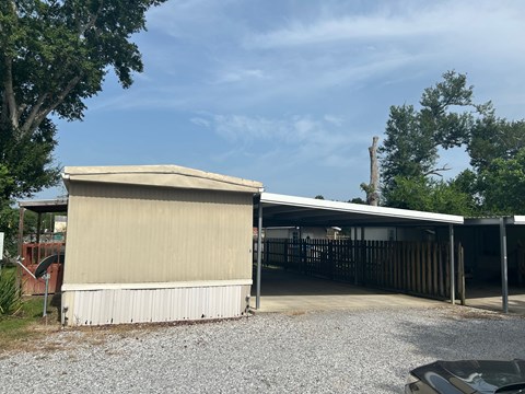 A carport with a tan roof is situated in a gravel driveway.