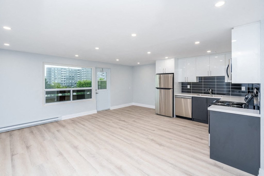 an empty living room with a kitchen and a window