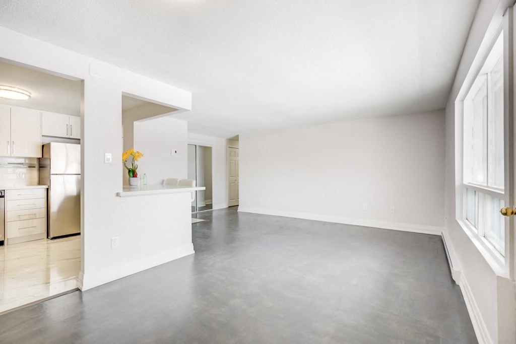 an empty living room and kitchen with white walls and a concrete floor