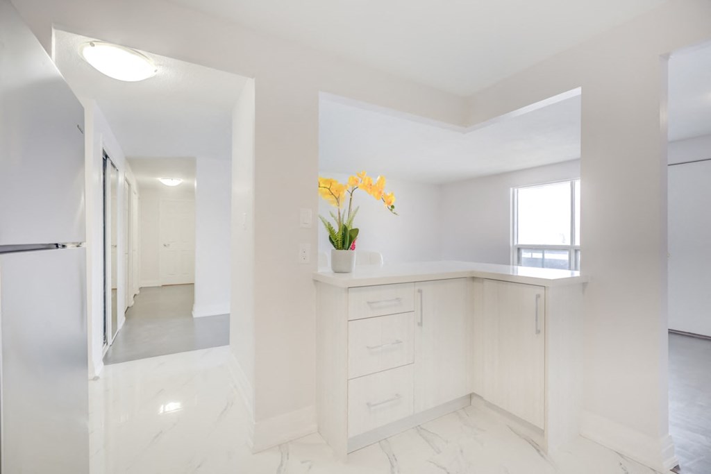 a white kitchen with white cabinets and a yellow flower in a vase