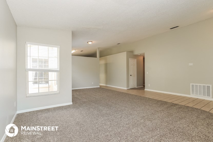 the spacious living room and dining room with white walls and carpet