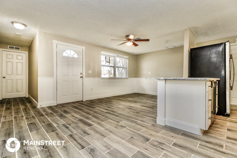 an empty living room with a kitchen and a ceiling fan